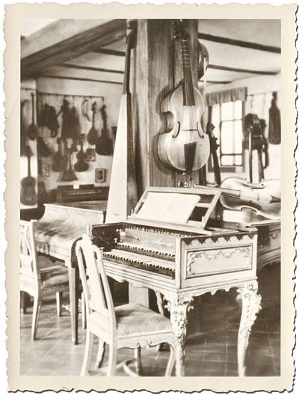 Schwarzweiß mit weißem Riffel-Rand und alt: Im Steckbrief-Foto sieht man ein Cembalo, ein Klavier und viele Streichinstrumente an den Wänden: Alle spielte Johann Sebastian Bach.