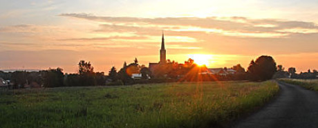 Das Bild im Kapitel Ursprung zeigt Wechmar mit einem grünen Feld im Vordergrund und rechts die gerade aufgehende Sonne neben dem Kirchturm. Es ist ein aktuelles Foto.