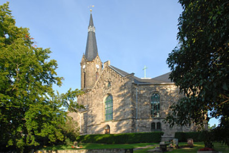 Ein Foto zum Ursprung Kapitel zeigt die Sankt Viti Kirche in Wechmar mit dem hohen Turm. Vorne sind Gräber, rechts und links zwei Bäume, die Ansicht ist von der Rückseite. Sonnenschein und wolkenlos.