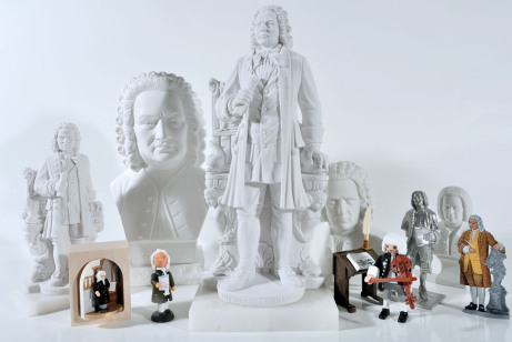 Es ist eine Art Gruppenaufnahme: Vor weißem Untergrund sind Bach-Büsten, Bach-Statuen, Bach-Zinnfiguren, Bach-Männchen aus Holz und die Kleine Bach-Figur aufgestellt.