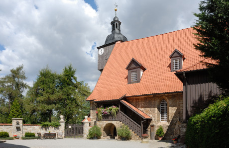 In der rechten Bildhälfte ist eine niedliche, kleine Kirche mit dem Kirchturm hinter dem Kirchenschiff. Links ist das Denkmal von Bach in Dornheim.