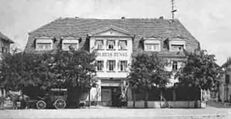 Es ist ein sehr unscharfes historisches Foto des Hotels Goldene Henne. Vor dem Hotel sind Bäume und man sieht eine Kutsche.