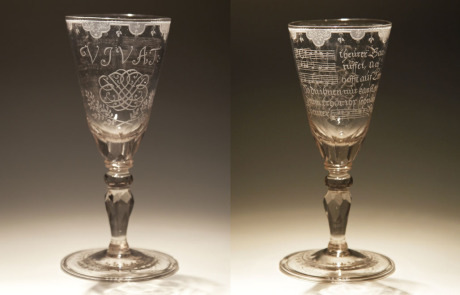 Zwei Fotos von zwei Kelchen, Trinkgefäßen, stehen vor einem weiß/braun verlaufenden Hintergrund. Auf der Vorderseite ist das Bach-Monogramm sichtbar, auf der Rückseite sind es Notenlinien mit Noten darauf.